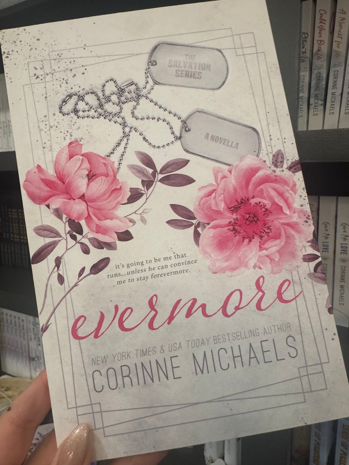 Book cover with the title "Evermore" by Corinne Michaels with pink floral design and dog tags held in a hand