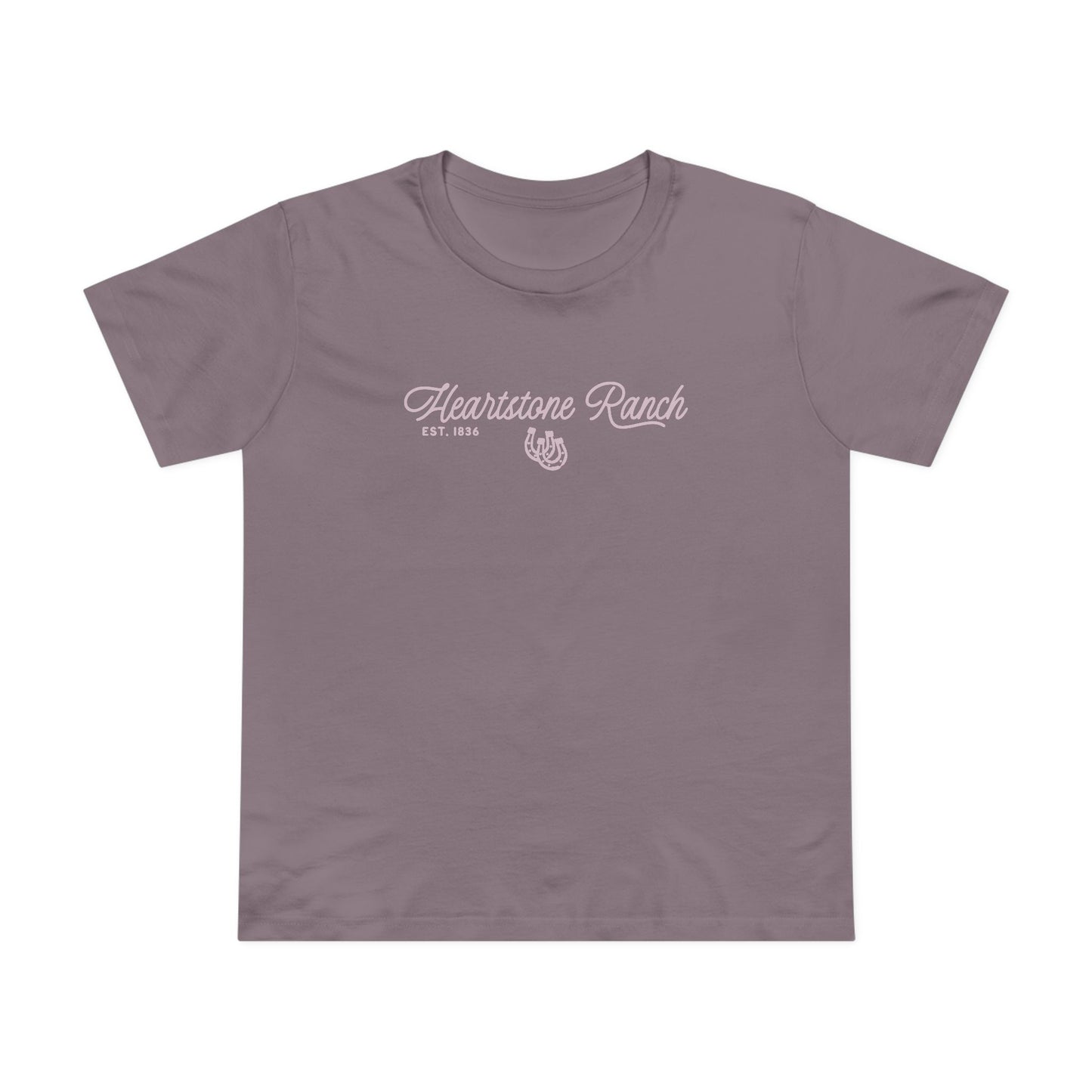 A mauve-purple short-sleeve t-shirt hanging on a light wood hanger against a white paneled wall. The shirt features a white screen-printed graphic on the chest reading 'Heartstone Ranch EST.