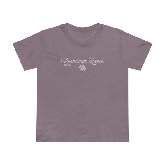A mauve-purple short-sleeve t-shirt hanging on a light wood hanger against a white paneled wall. The shirt features a white screen-printed graphic on the chest reading 'Heartstone Ranch EST.