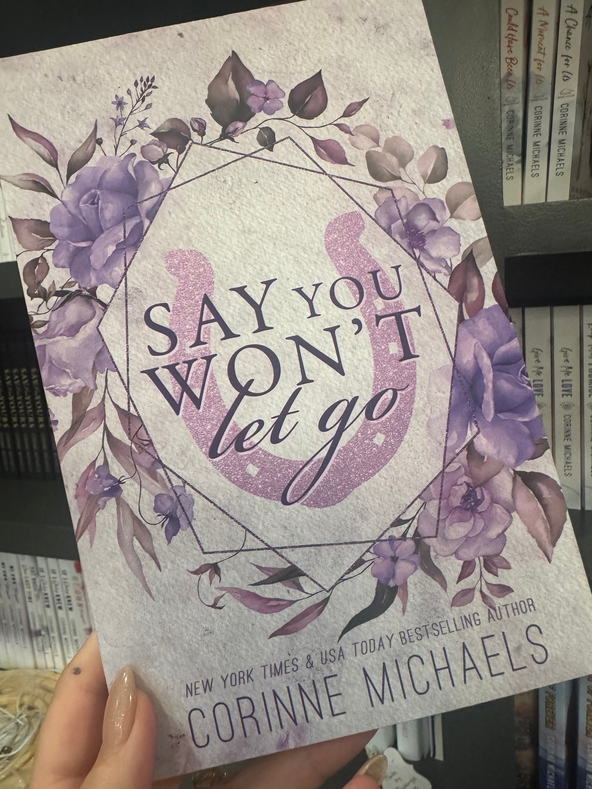 Book titled "Say You Won't Let Go" by Corinne Michaels with purple floral design held by a hand.