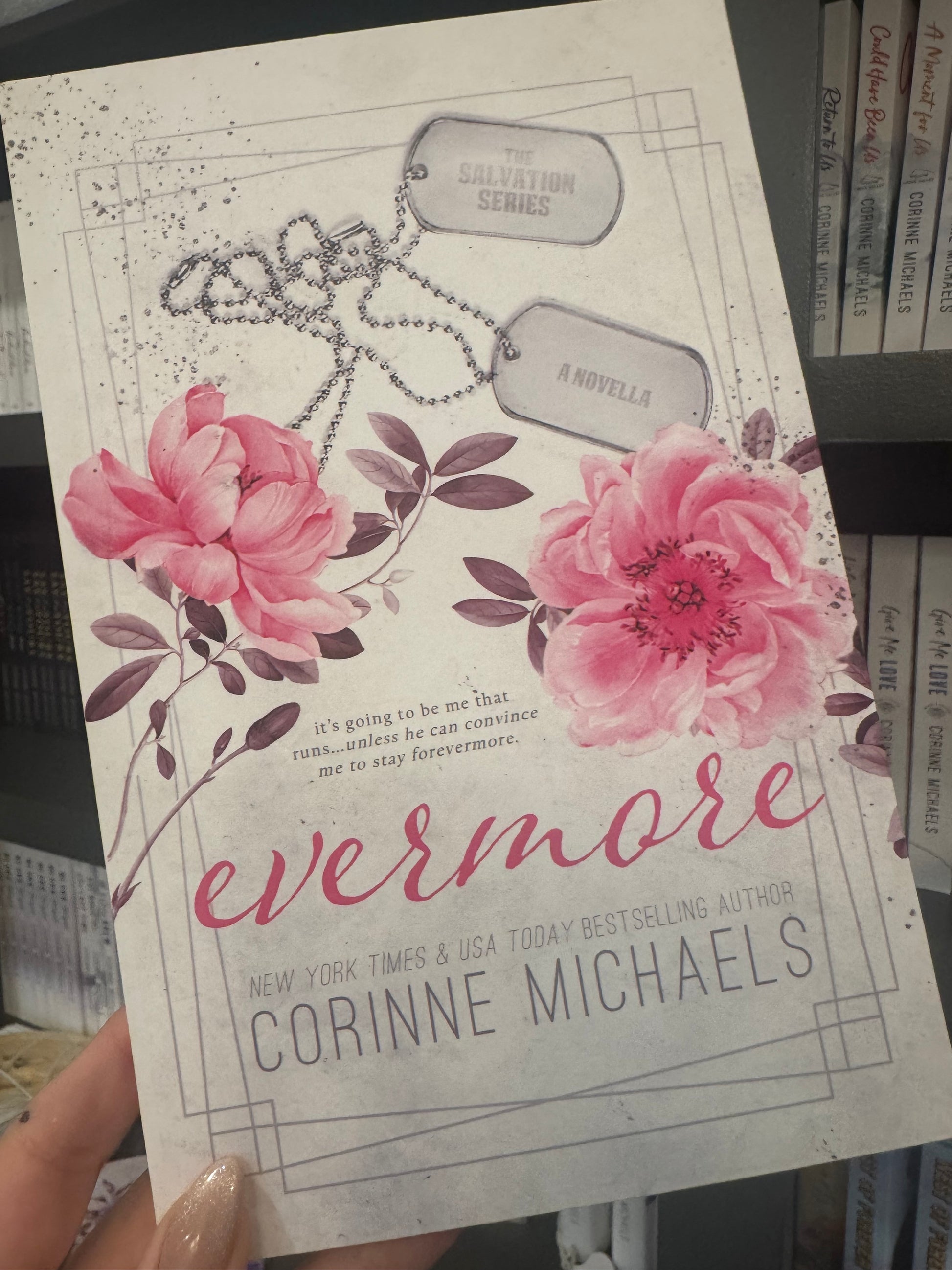 Book cover with the title "Evermore" by Corinne Michaels with pink floral design and dog tags held in a hand